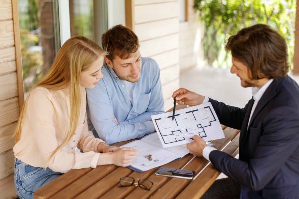 Real estate agent showing house plan to millennial couple at table on porch